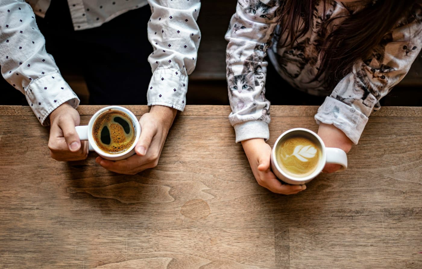 Two people holding coffee cups across a wooden table