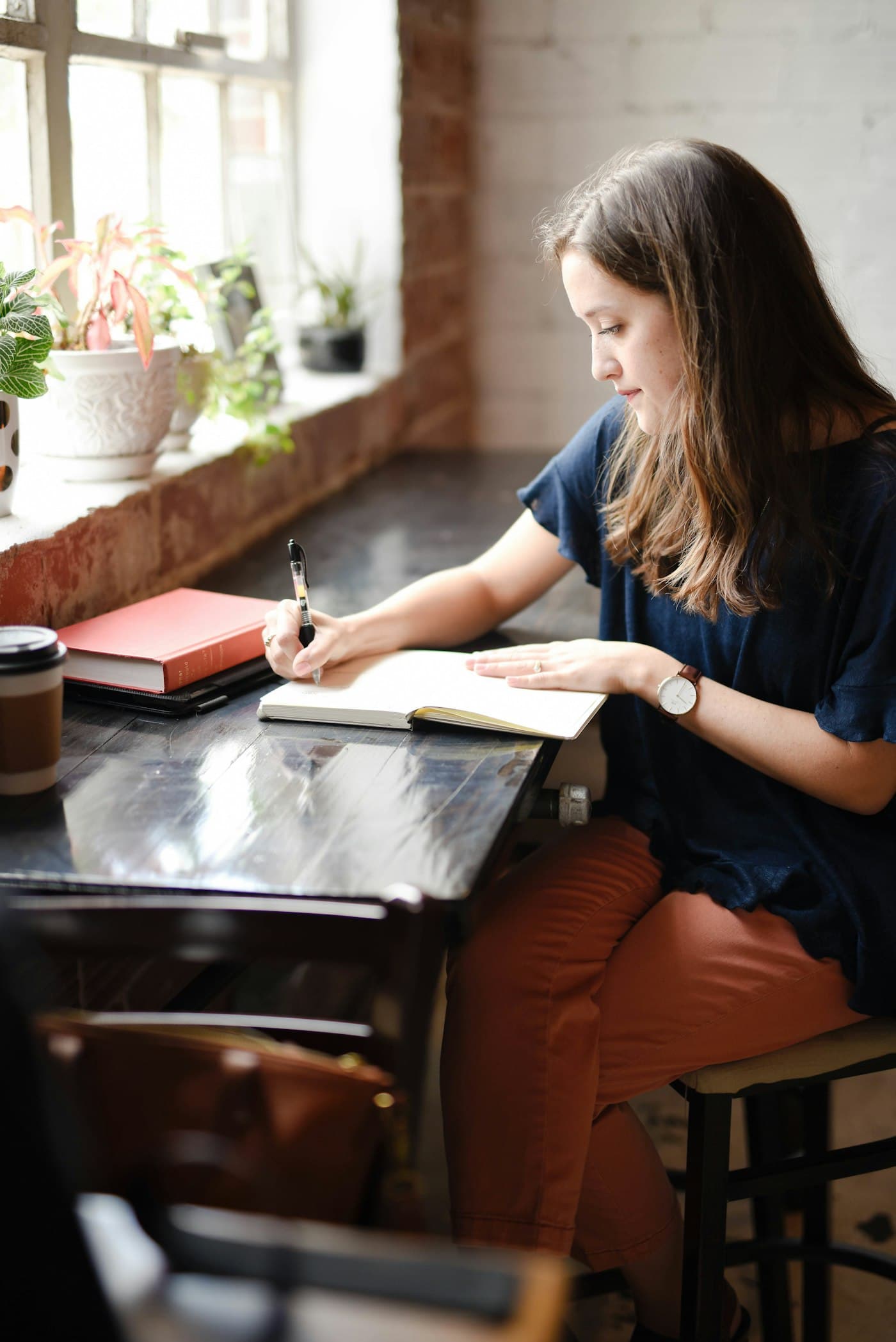 A woman writing in a notebook at a sunny window table