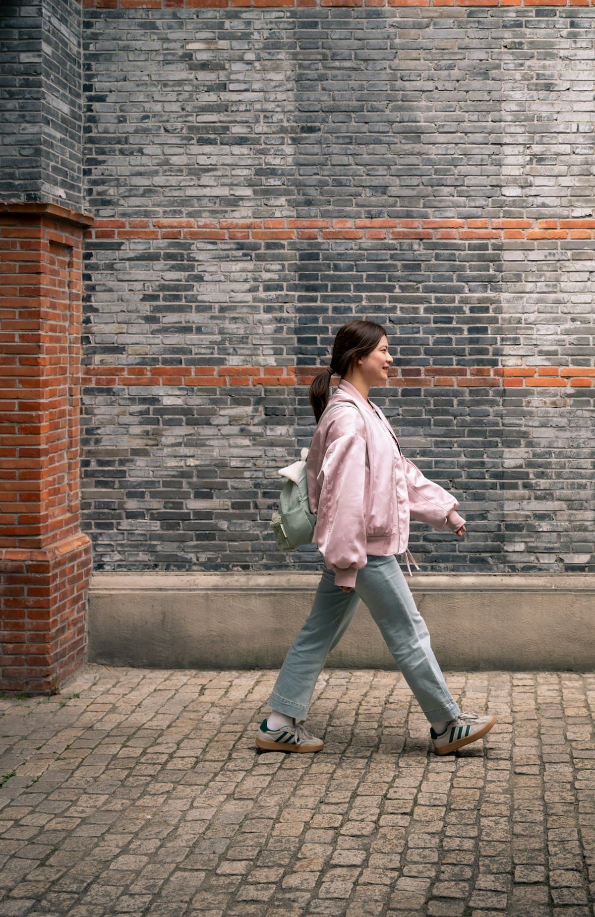A woman in a pink jacket walking past a brick wall