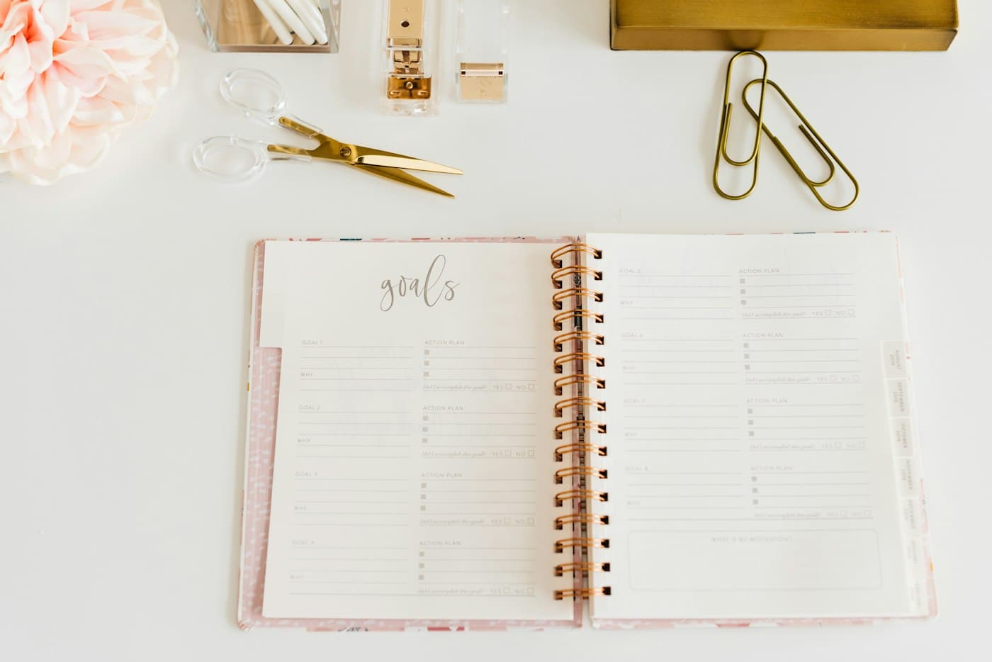 An open goals planner on a desk with paper clips and flowers